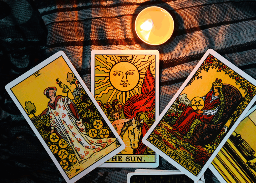 closeup image of three tarot cards with a little lamp light in the middle on top of cloth